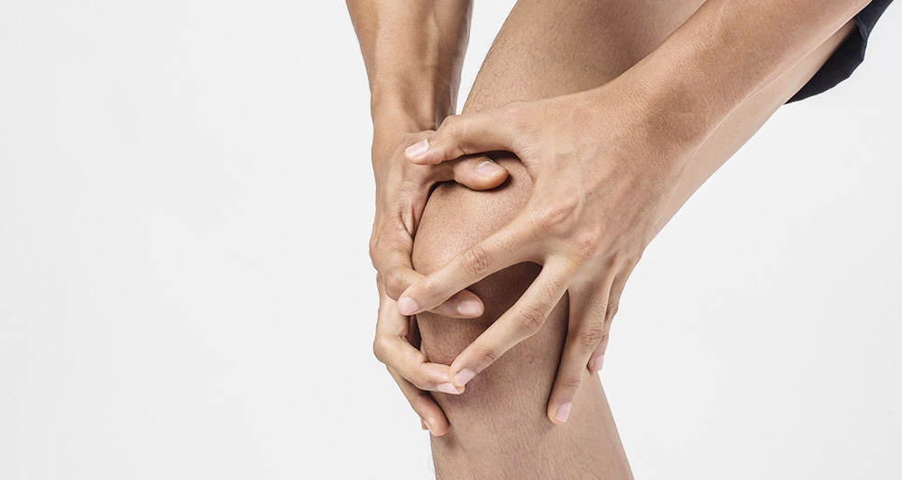 Young sport man with strong athletic legs holding knee with his hands in pain after suffering ligament injury isolated on white.